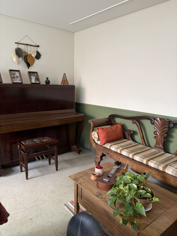 Sala da casa com piano de madeira, sofá antigo, plantas e parede verde até meia altura.